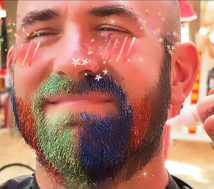 Glitter on Face Ideas: 19 Looks, From Freckles to Skulls 4 Man with a beard decorated in green, blue, and red glitter.