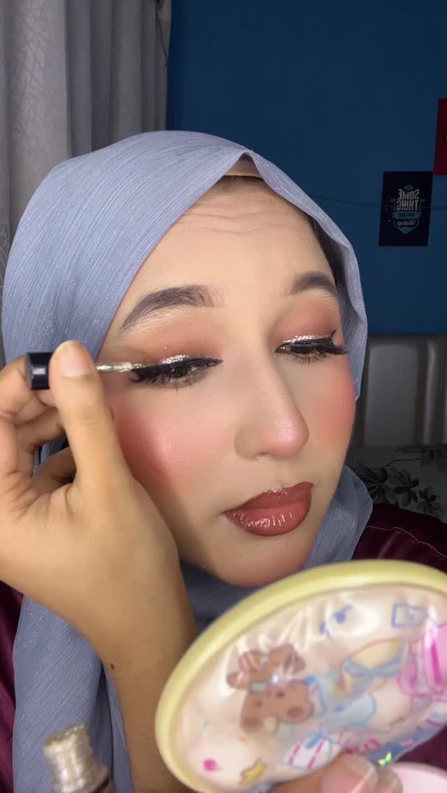 Glitter on Face Ideas: 19 Looks, From Freckles to Skulls 9 Woman in blue hijab applying silver glitter eyeliner to her upper eyelid.