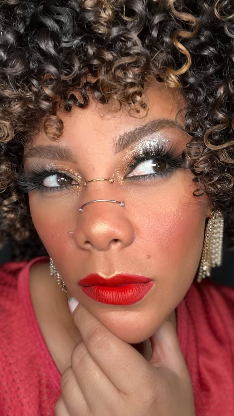 Glitter on Face Ideas: 19 Looks, From Freckles to Skulls 14 Woman with curly hair, red lipstick, and gold glitter eyeshadow wearing nose rings.