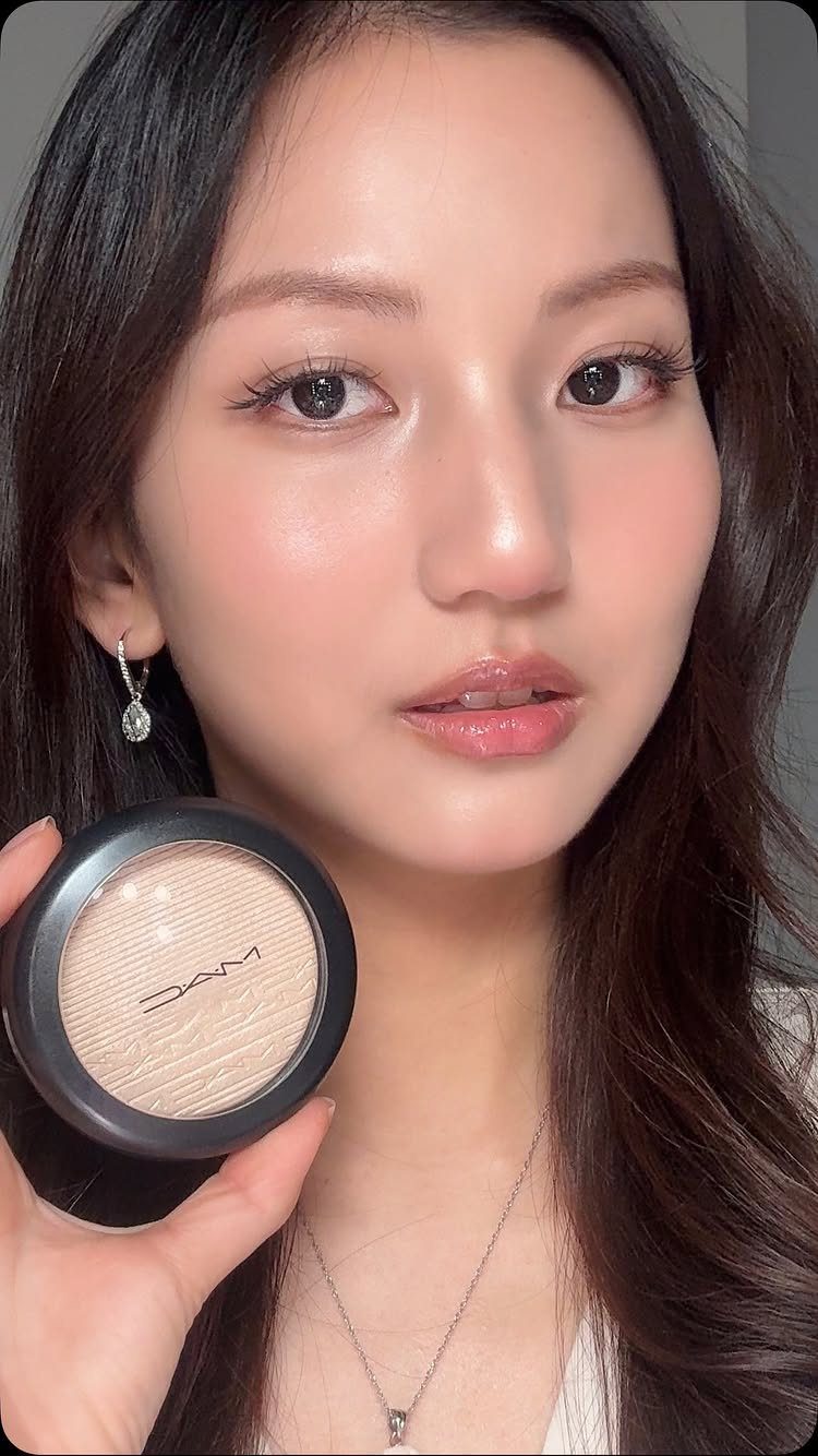 Woman with glowing makeup holding a MAC highlighter compact near her face