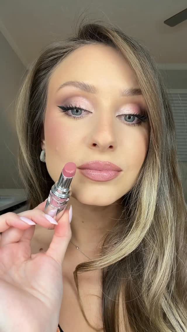 Woman applying pink lipstick to her lips as part of a makeup look.
