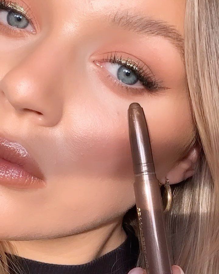 How to Do Makeup for Big Eyelids: 7 Ideas to Try 2 Woman with gold shimmery eyeshadow and glossy lips holding a makeup pencil.