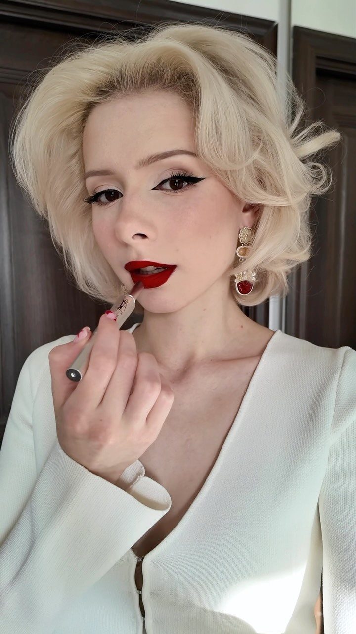 Blonde woman with blue eyes wearing bold cherry red lipstick and winged eyeliner.