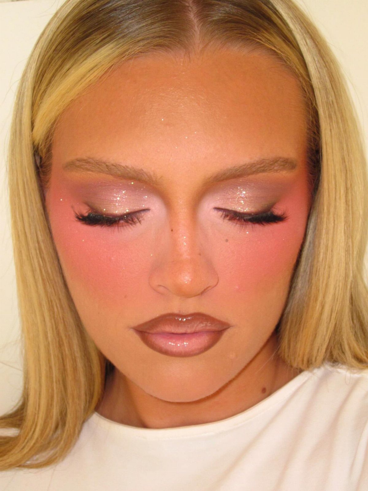 Woman with blonde hair wearing pink eyeshadow and peachy-pink blush on her cheeks