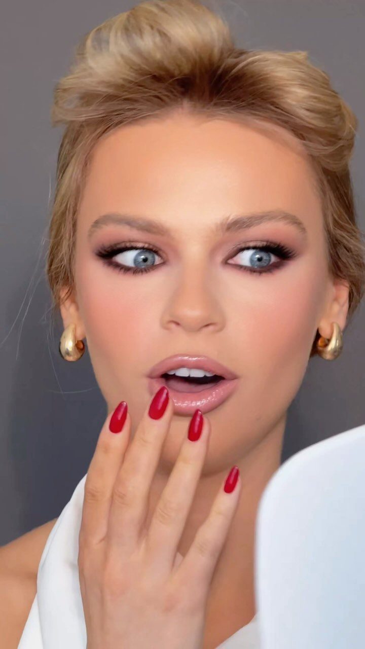 Woman with blonde hair and blue eyes wearing smoky eye makeup and red nails