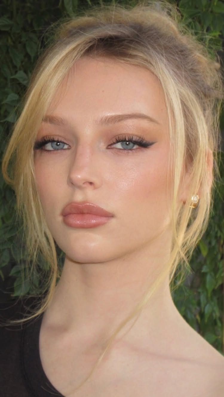 Woman with blonde hair and blue eyes wearing winged eyeliner and neutral lipstick.