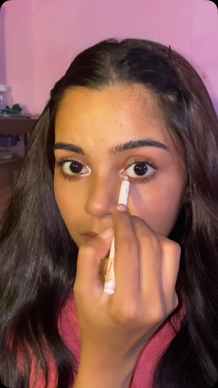 Makeup for Eye Bags: 3 Ideas for a Smoother Look 3 Woman applying concealer under her eye with a small white makeup applicator brush.