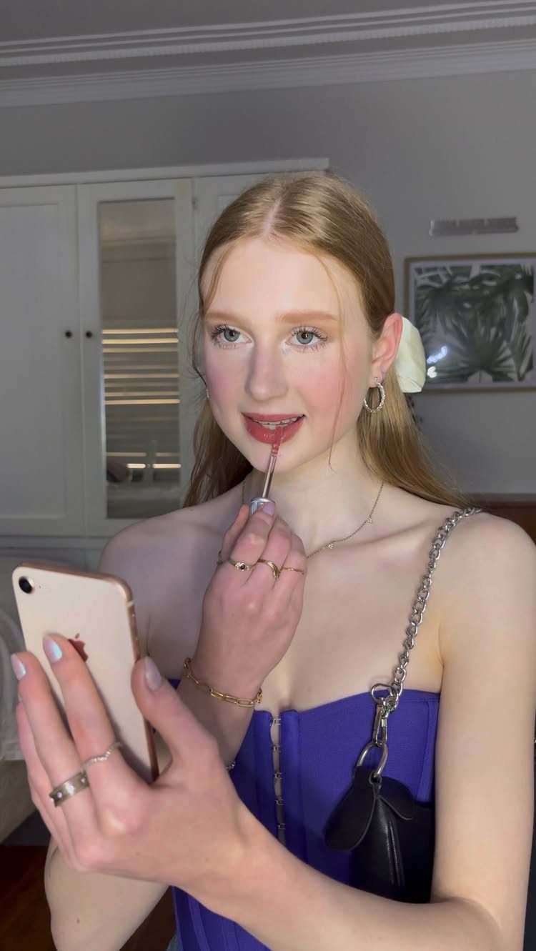 Makeup for Pale Skin and Blue Eyes: 6 Looks to Try 5 Pale-skinned woman with blue eyes applying pink lip gloss while taking a selfie.