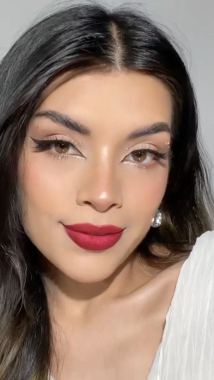 Woman with matte red lips, winged eyeliner, and glittery eyeshadow posing for portrait