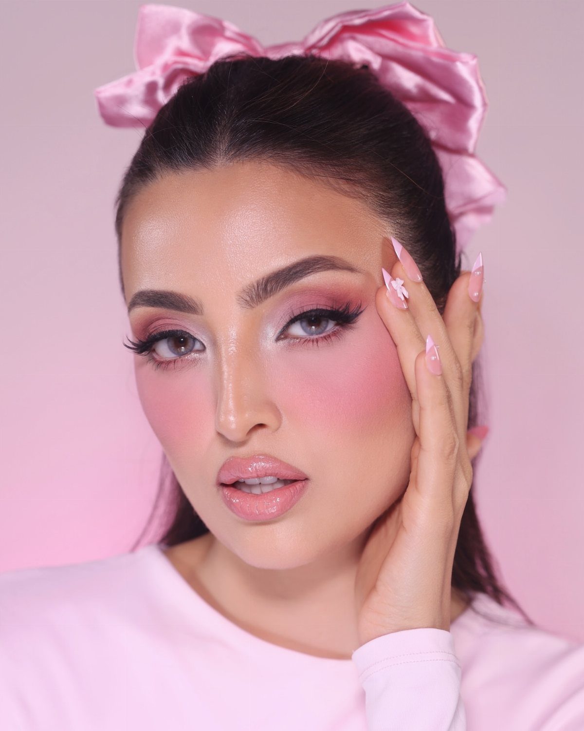 Woman with pink pastel eyeshadow and blush wearing a large pink hair bow.