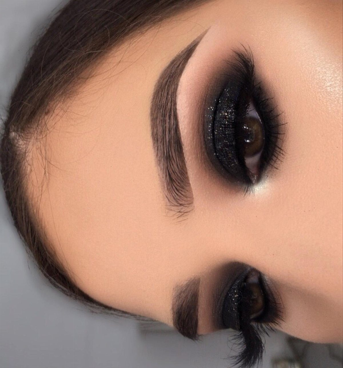 Bold black smokey eye makeup with glitter and defined arched eyebrows.