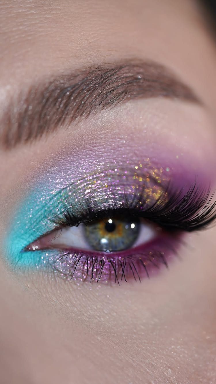 Eye with purple and teal jewel-toned eyeshadow, gold glitter, and long false lashes.