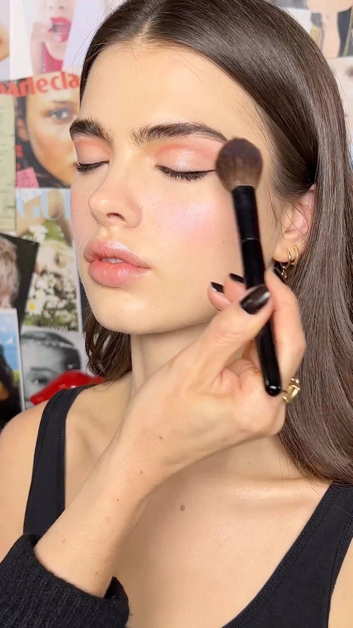Woman receiving blush application with peach eyeshadow and glossy lips.