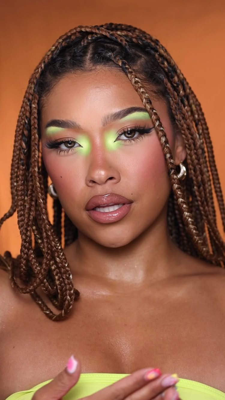 Woman with brown braids wearing bright neon green eyeshadow and glossy nude lips.