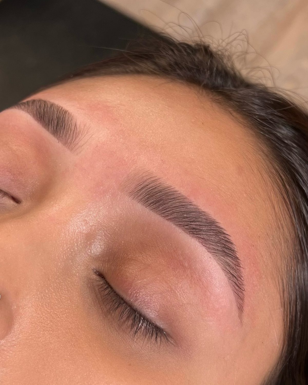 Closed eyes with brown eyeshadow and neatly groomed, defined brown eyebrows.