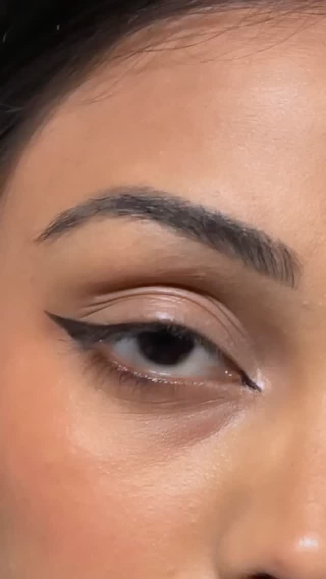 Eye with sharp black winged eyeliner and neutral brown eyeshadow and groomed eyebrows
