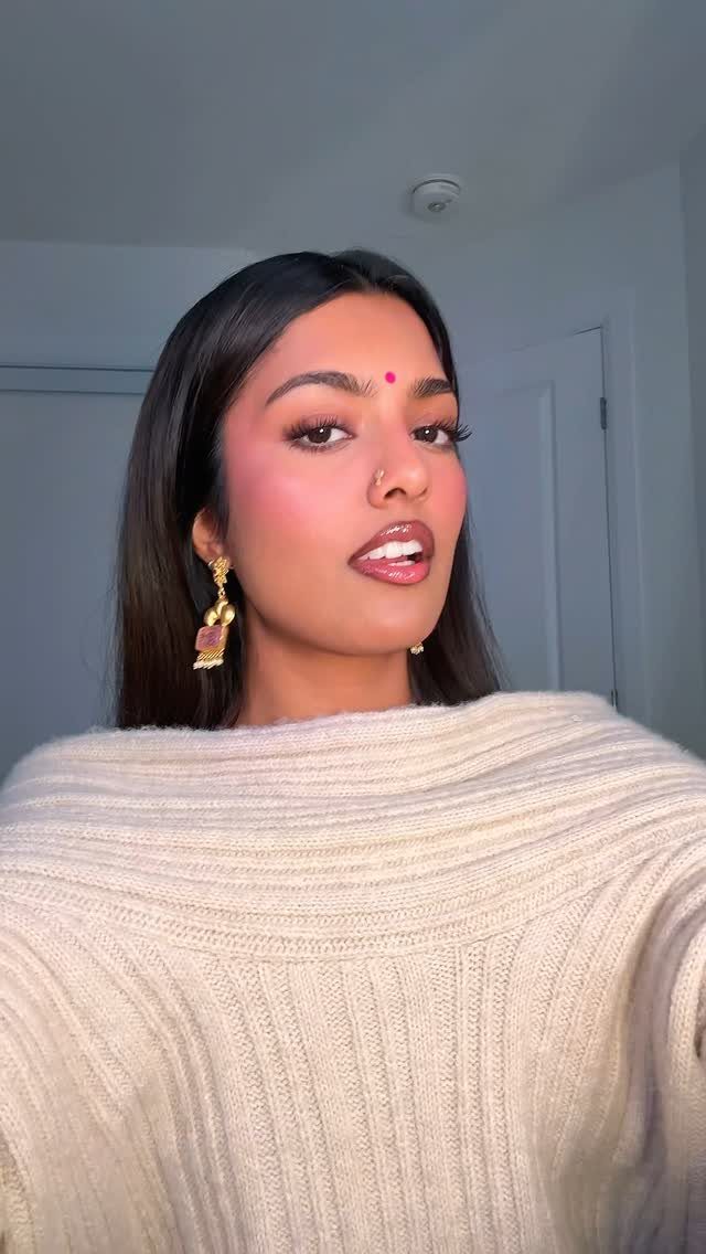 Woman with brown skin wearing berry blush, neutral makeup, and a beige sweater.