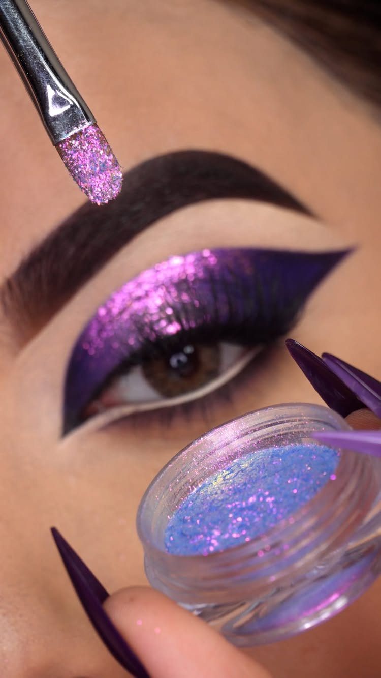 Person with brown skin wearing dramatic purple glitter eyeshadow and long purple nails.