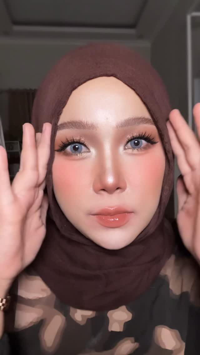 Woman with brown skin wearing peach-toned makeup and a brown hijab.