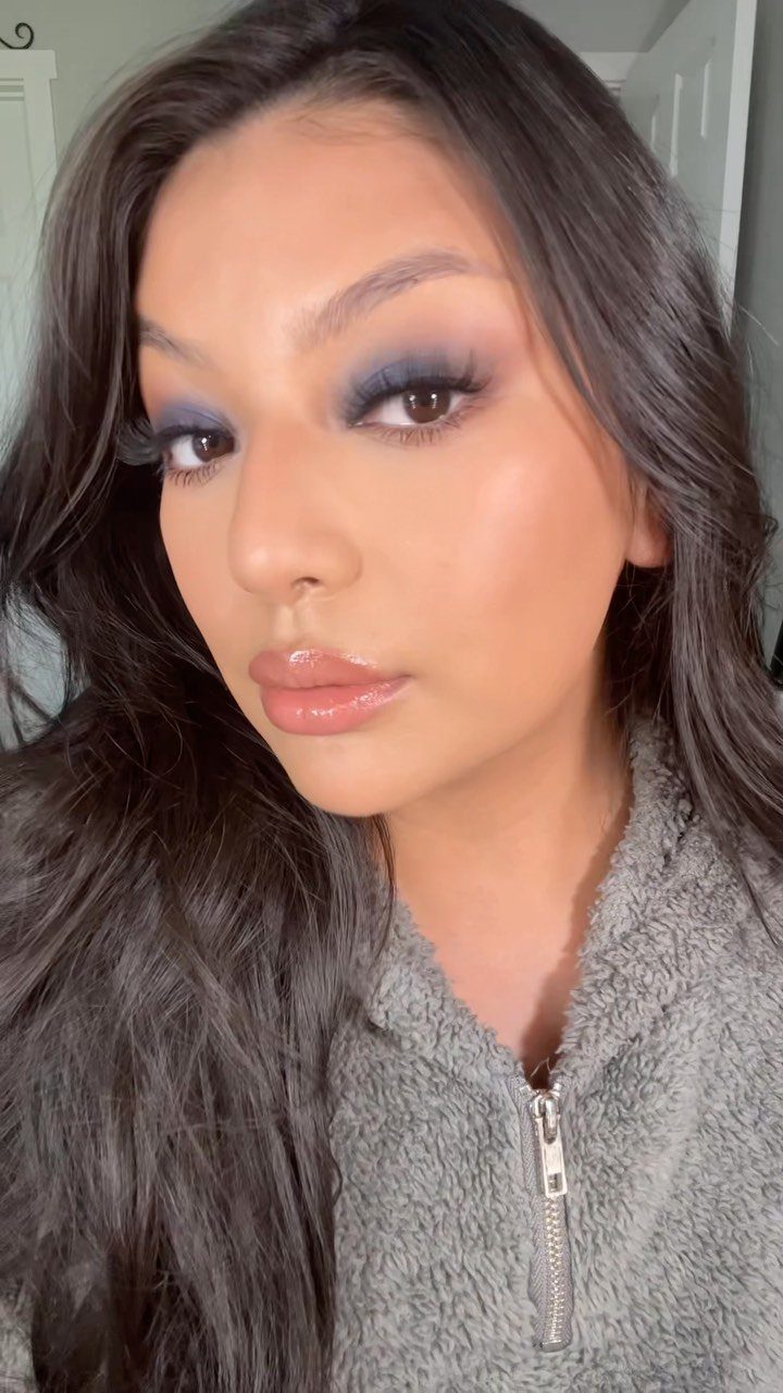 Woman with dark skin wearing blue eyeshadow and glossy lips in a portrait.
