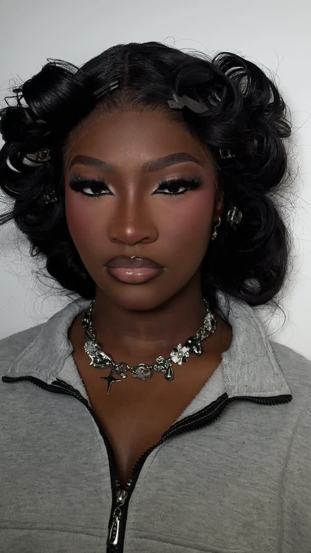 Woman with dark skin wearing a full glam makeup look and curly hair.