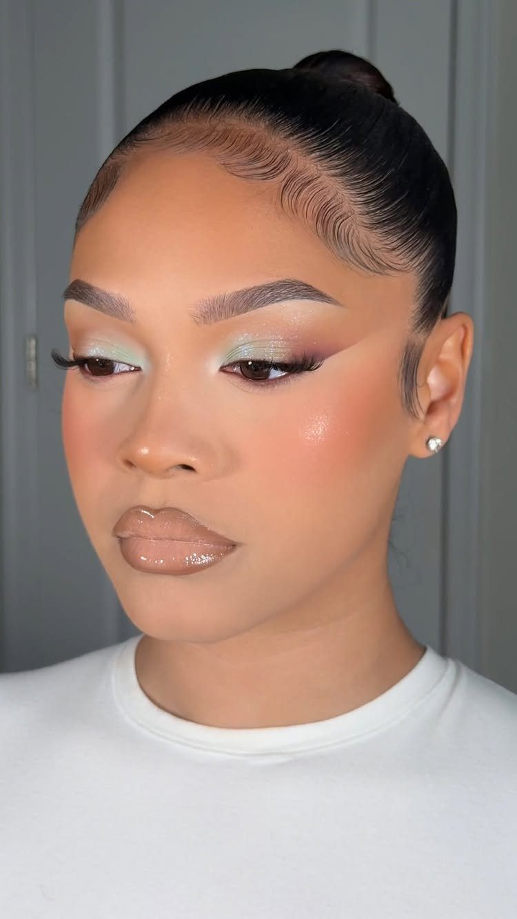 Woman with dark skin wearing light green eyeshadow and glossy nude lips.