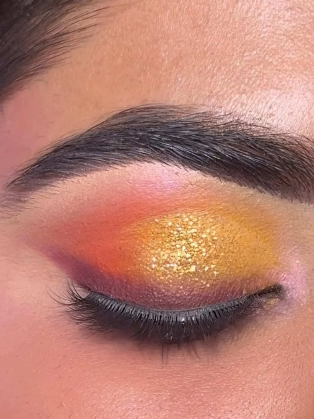 Eye with dark skin featuring orange and purple eyeshadow and gold glitter shimmer.