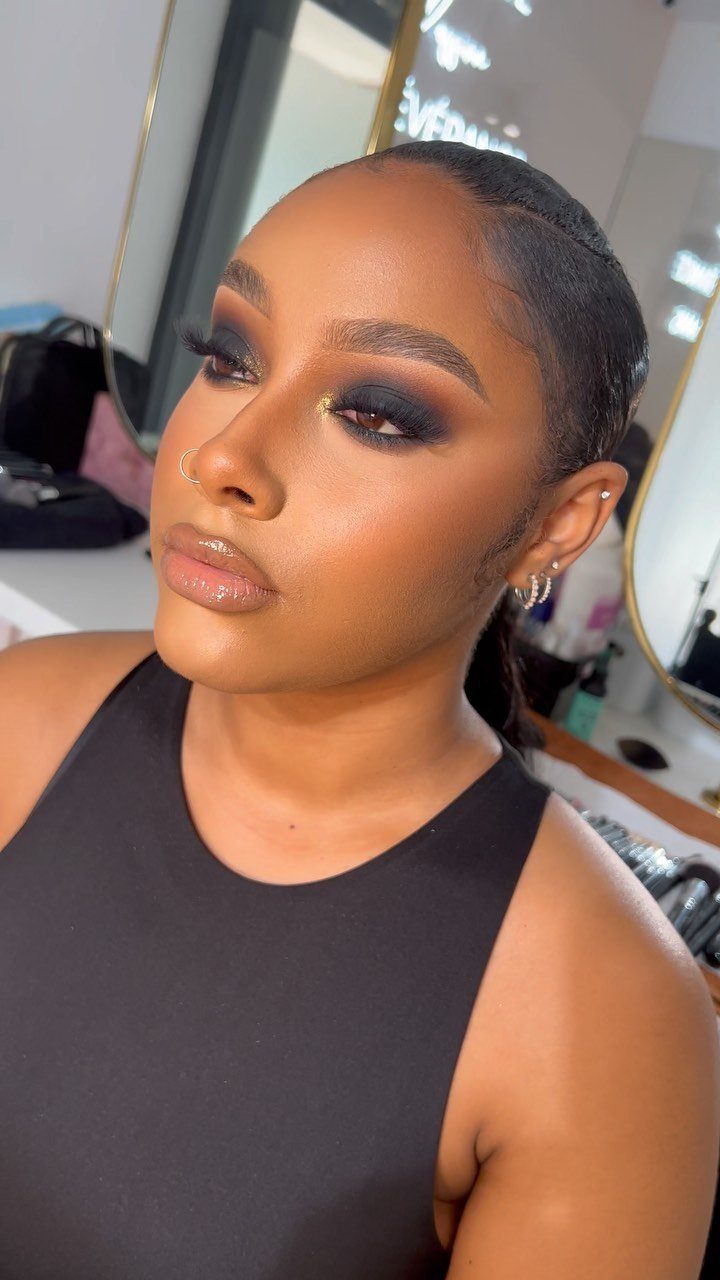 Woman with dark skin wearing a dark smoky eye and nude glossy lips.