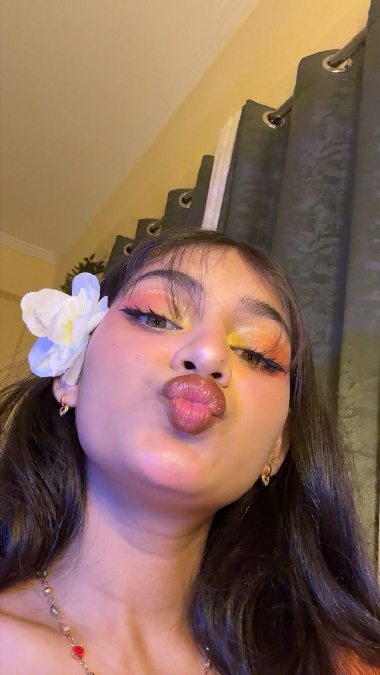 Woman with dark skin wearing bright orange eyeshadow and a white flower in hair