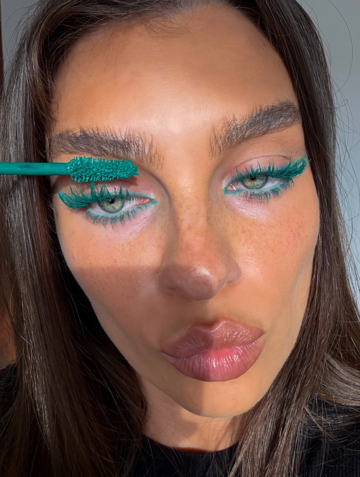 Woman applying teal mascara to her eyelashes for a bold makeup look.