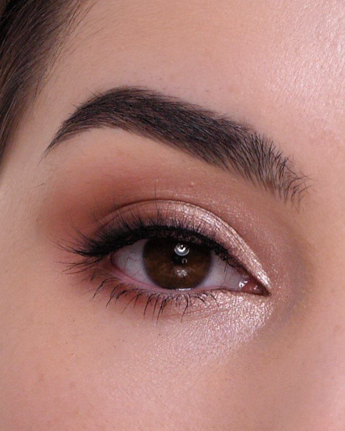 Close-up of an eye with shimmering peach eyeshadow and defined black lashes.