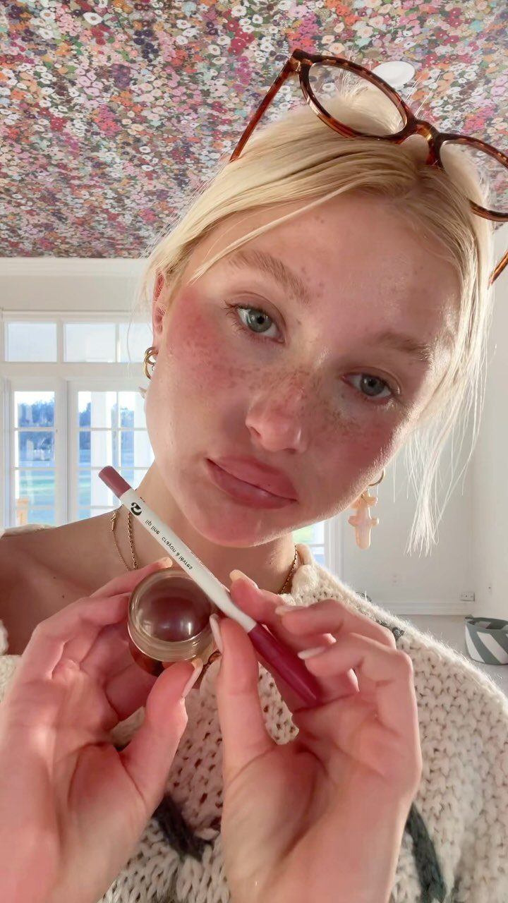 Blonde woman with radiant skin holding cream blush and a lip pencil.
