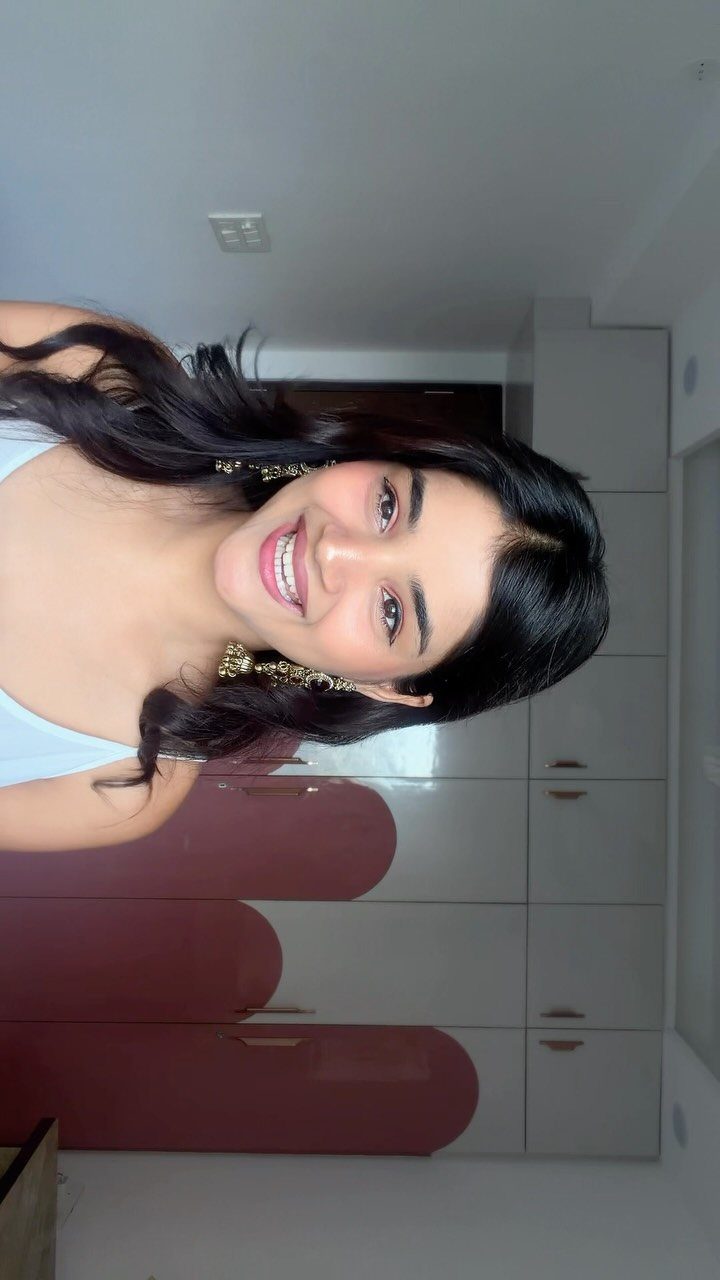 Smiling woman with long dark hair wearing minimalist makeup and gold earrings.