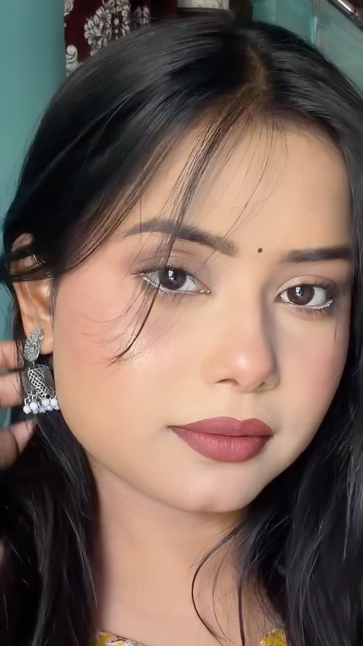 Woman with soft pink makeup, mauve lips, and silver traditional Indian earrings.
