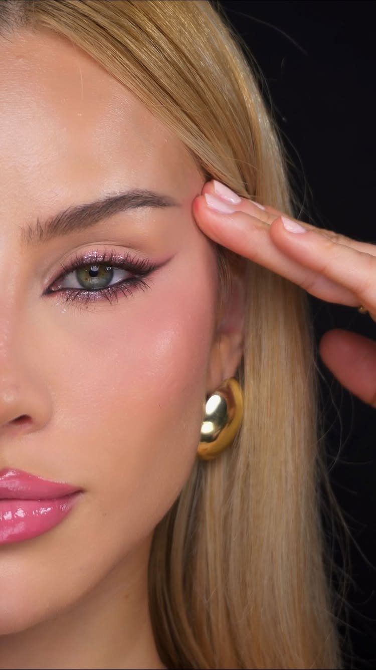 Woman with blonde hair wearing pink shimmering eyeshadow and black winged eyeliner.