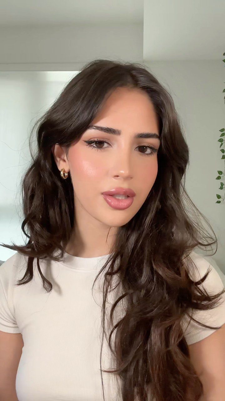 Woman with long wavy brown hair wearing polished soft glam makeup and white shirt