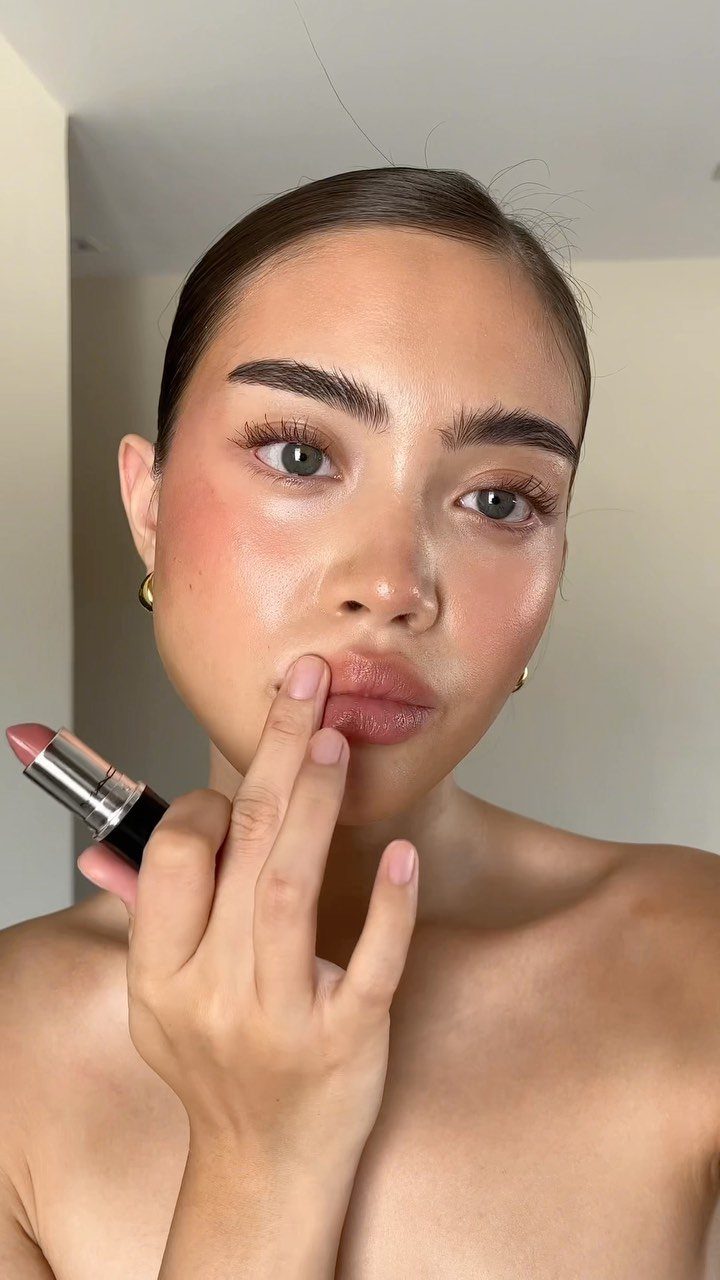 Woman with glowing makeup applying lipstick to her lips with her finger