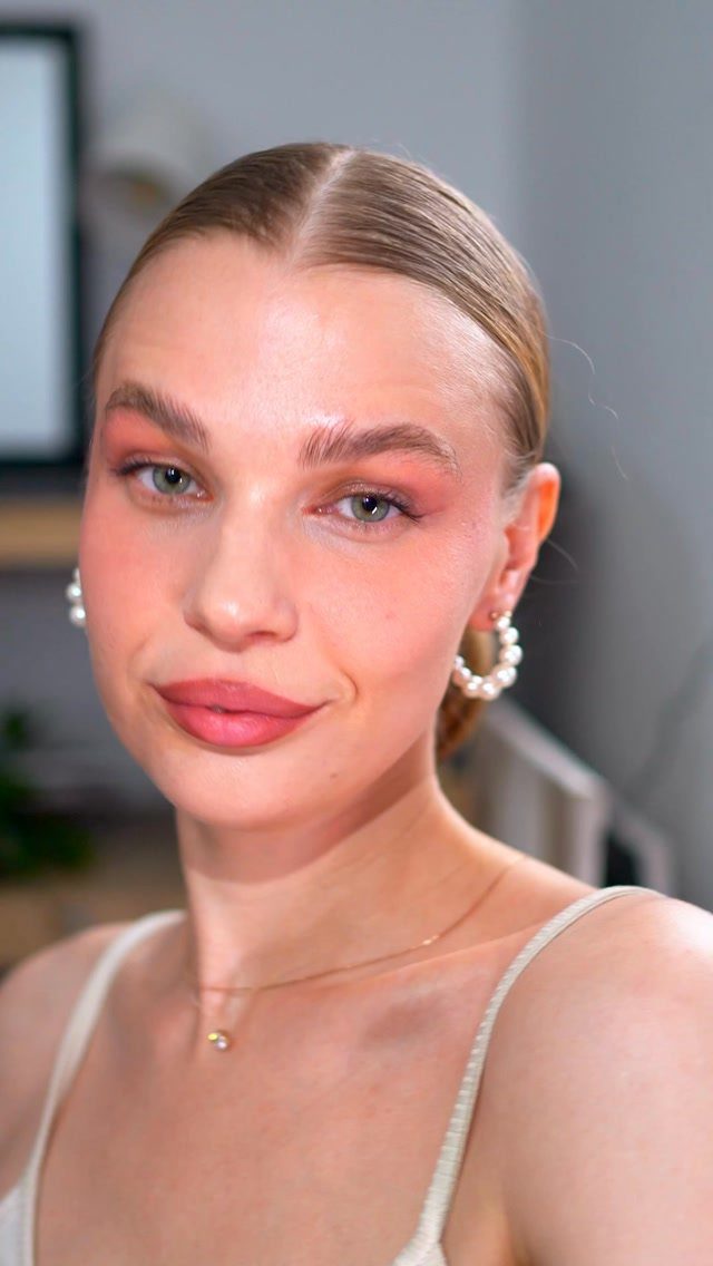 Woman with luminous skin, pink eyeshadow, and pearl earrings posing for a portrait.