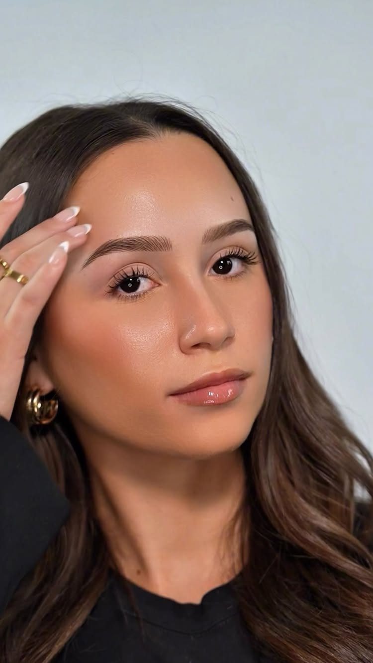Woman with groomed natural eyebrows and glowing makeup posing against a grey background