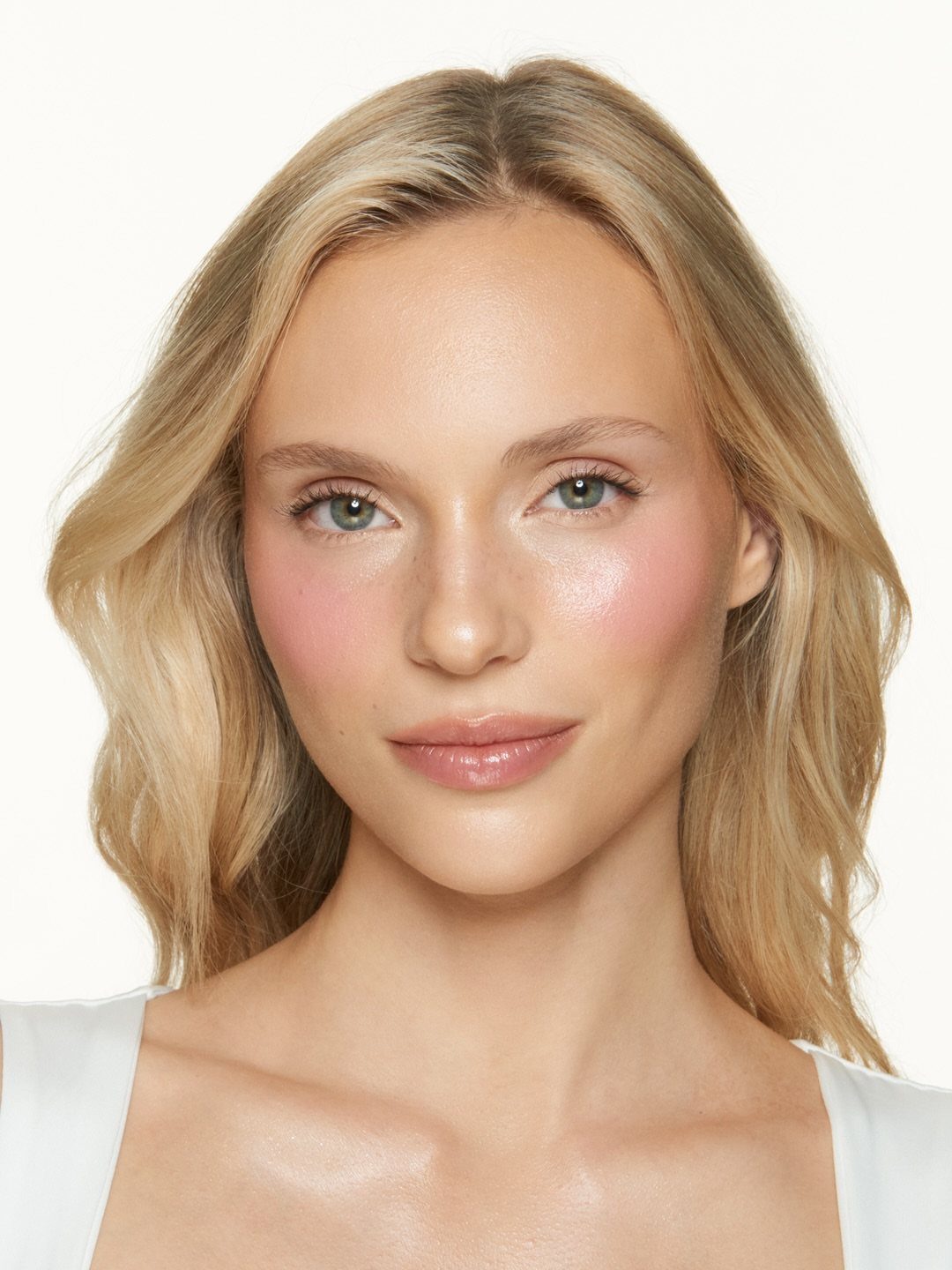 Blonde woman with glowing skin, pink cheeks, and glossy lips on white background