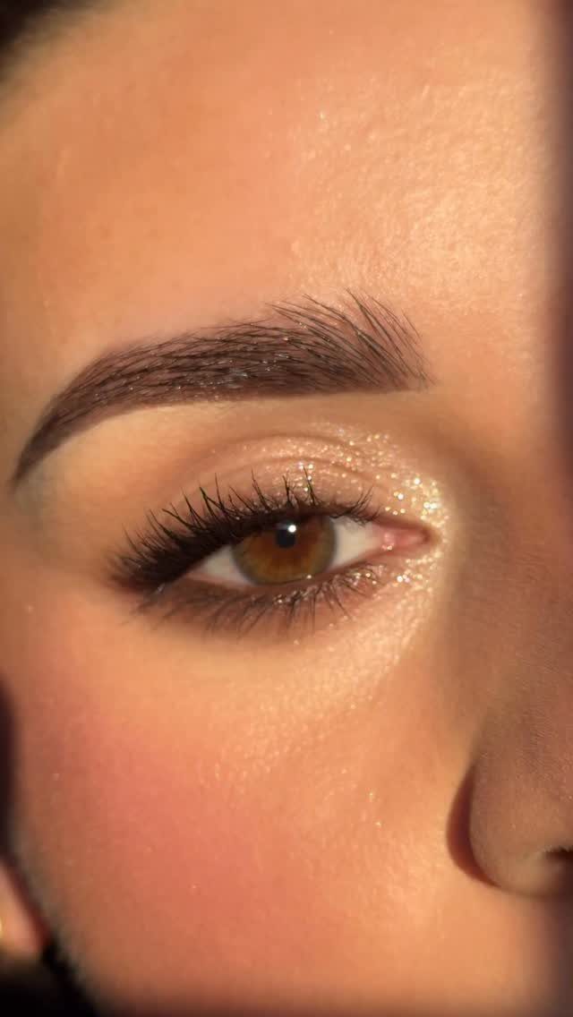 Close-up of an eye with shimmering gold eyeshadow and groomed natural brows.