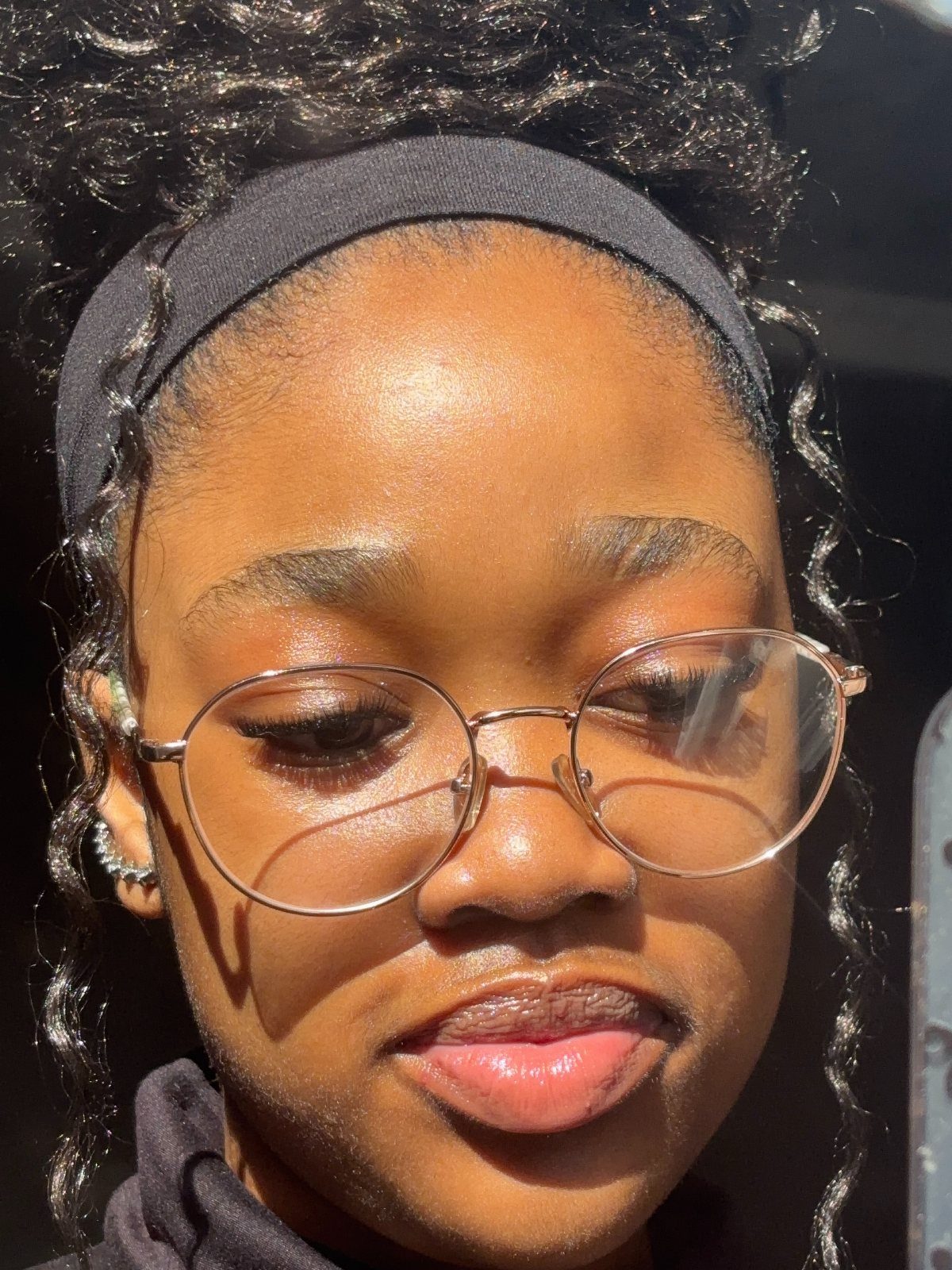 Person with glowing skin, gold glasses, and glossy pink lips wearing a headband.
