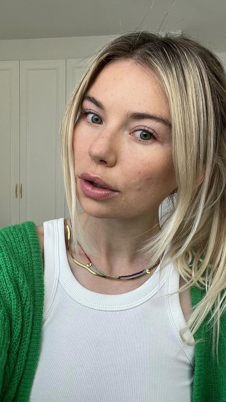 Blonde woman with natural makeup wearing a white top and green cardigan.