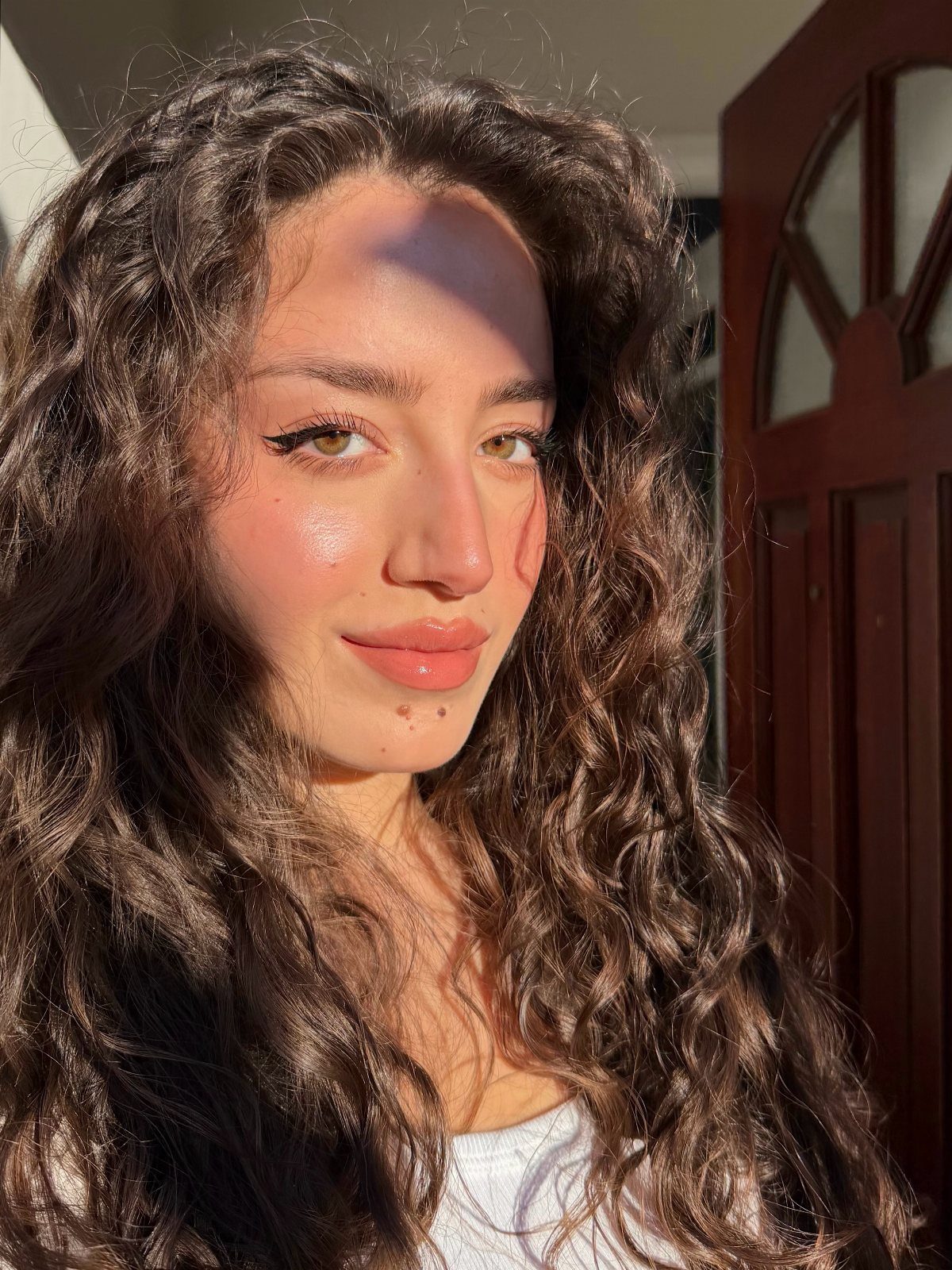 Woman with curly brown hair wearing a subtle, glowing natural makeup look.
