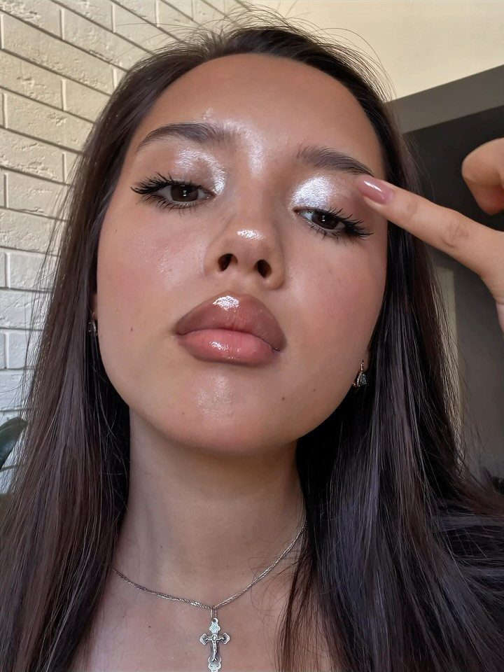 Woman with glowing skin, shimmering eyeshadow, and glossy lips posing for a portrait.