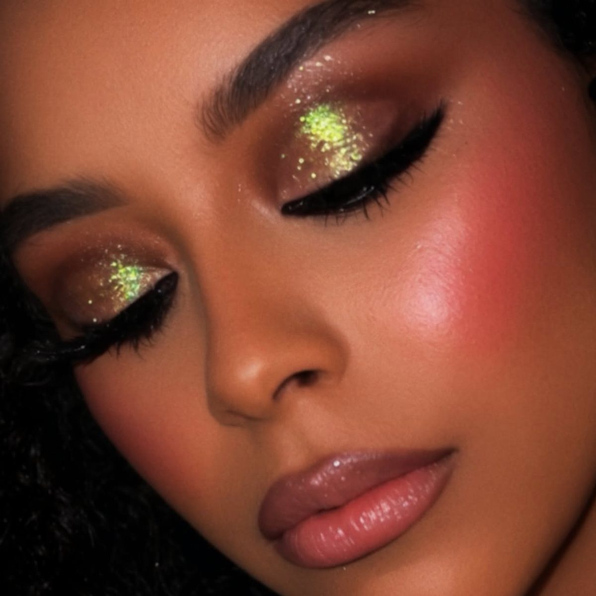Person with gold shimmer and lime green glitter eyeshadow and winged eyeliner.