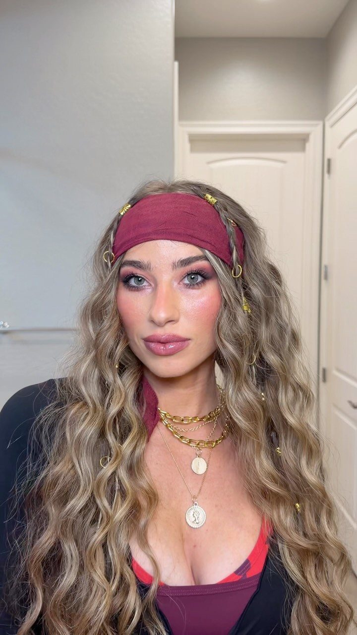 Woman in pirate attire with a red headband and gold layered necklaces.