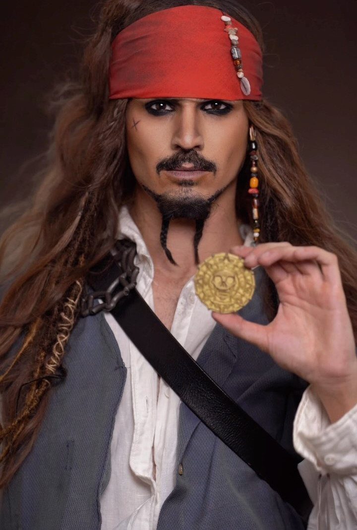 Pirate with heavy black eyeliner, braided goatee, and red headband holding gold coin