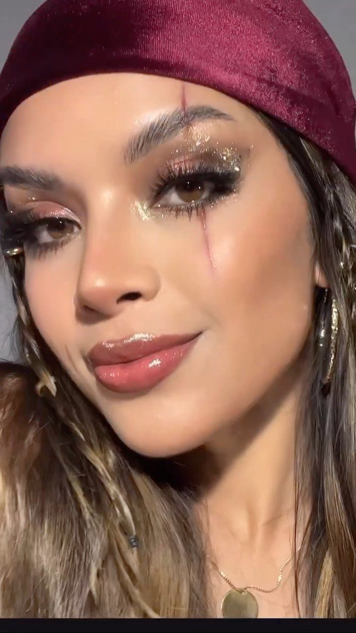 Woman with glittery gold eyeshadow and a red scar makeup line wearing a headscarf