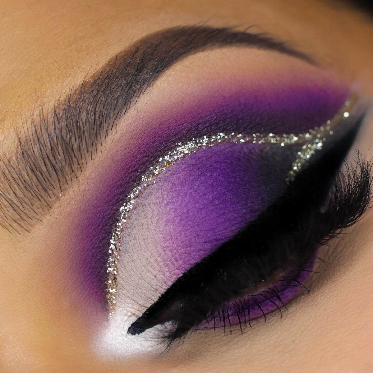 Purple eyeshadow with gold glitter and black winged eyeliner on a closed eye